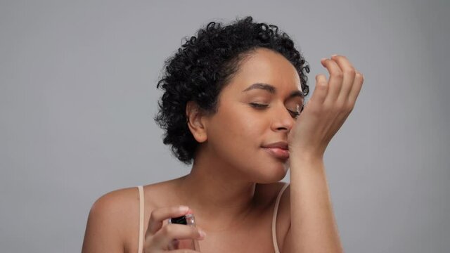 beauty, perfumery and people concept - portrait of happy smiling young african american woman with bare shoulders applying perfume to her wrist over white background