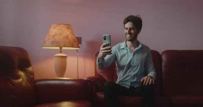 Ragazzo si fa i selfie con lo smartphone mentre &egrave; seduto sul divano di casa
