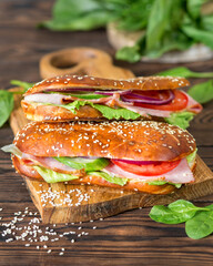 A delicious snack. Sandwich with tomatoes, spinach and ham. Aperitif on a wooden background. A sesame bun. American cuisine. Fresh food.