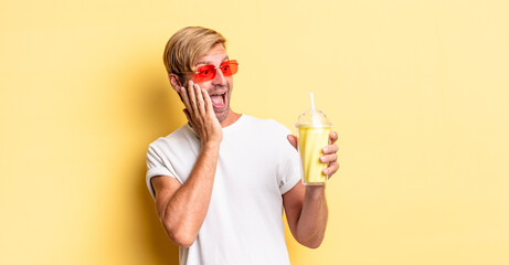 blond adult man feeling happy, excited and surprised with a milkshake