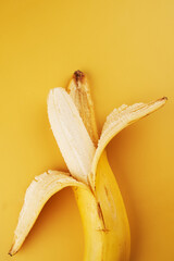 Whole half peeled banana isolated on yellow background close up