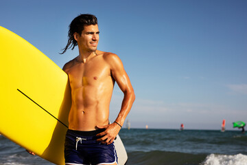 Portrait of handsome surfer with his surfboard. Young man with a surfboard on the beach.