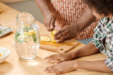 Little boy standing by his father slicing fresh lemon while making homemade lemonade