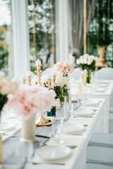 White long set wedding dinner table with decoration, candlestick, glasses, and flowers. Selective focus.