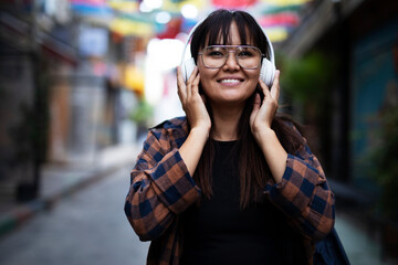 Fototapeta premium Young smiling woman outdoors. Beautiful woman listening to music while walking through the city