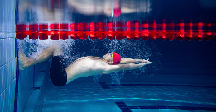 At start. Sportive male swimmer in red cap and goggles in motion and action during training at pool, indoors. Healthy lifestyle, power, energy, sports movement concept