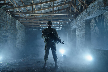 Portrait of airsoft player in professional equipment with machine gun in abandoned ruined building....