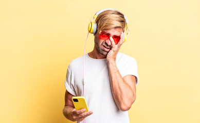 blond adult man feeling bored, frustrated and sleepy after a tiresome with headphones