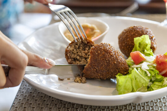 Closeup shot of a female slicing a piece of cutlet with a green salad on a plate