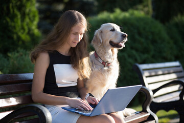 Young beautiful business woman working on a laptop sitting on the bench in the street with her dog