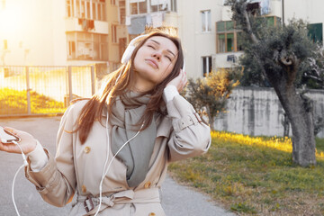 Caucasian Young Girl Listening Track or Podcast With White Over-Ear Headphone In Green Public Garden. Leisure Meditation for Calming Down and Relaxing. Mindfulness and Music Therapy.