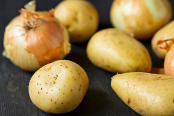 Raw potatoes and onions on a black background