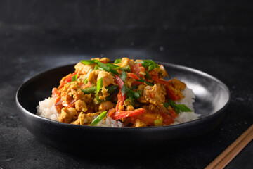 Thai dish Gai Pad Pongali with chicken, eggs, spicy, yellow thai curry paste,tomato, rice in black bowl made in wok. Close up. Traditional local breakfast. Thai Food Stir Fried.
