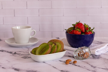 Kiwi en un recipiente en primer plano acompañada de frutillas y  almendras sobre una tabla de madera, concepto de alimentación saludable y vegana.