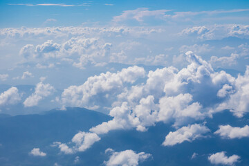Aerial view scene of the mountain which hiding under white fluffy clouds and blue bright sky background.