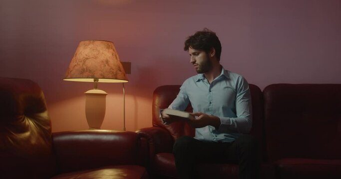 Giovane ragazzo seduto sul divano legge un libro la sera