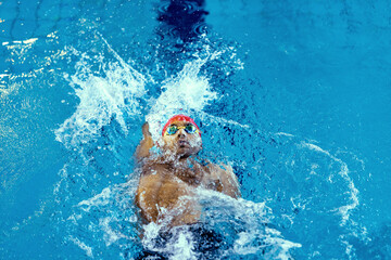 Top view of professional male swimmer in goggles practicing and training at pool, indoors. Healthy lifestyle, power, energy, sports movement concept