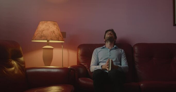 Giovane ragazzo seduto sul divano legge un libro la sera