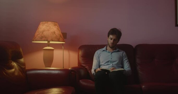 Giovane ragazzo seduto sul divano legge un libro la sera