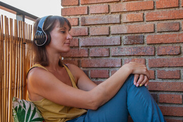 Mujer sentada en la terraza de su casa en el sofá hecho por palets escuchando música con sus...