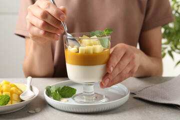 Woman eating delicious panna cotta with mango at table, closeup