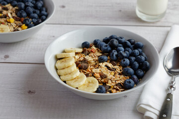 Fruit muesli with fresh blueberries and banana slices in a porcelain bowl. Table view.
