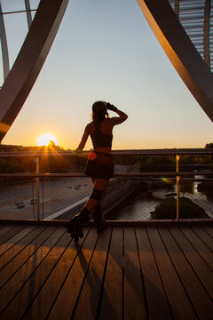 Chica patinadora en l&iacute;nea patinando en un puente de Madrid Rio.  Mujer con accesorios de roller. Chica skate mirando desde un puente el atardecer. Mujer a contraluz. Roller en atardecer. 