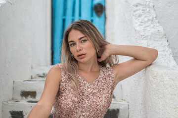 Fototapeta premium Close up portrait of beautiful caucasian girl with attractive blue eyes in casual summer dress. Sitting outdoors. Hand near her neck.