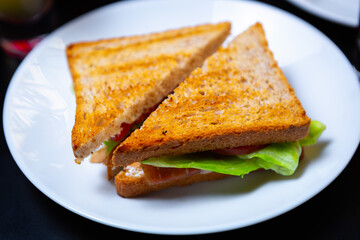 Club sandwich with fresh vegetables and lettuce salad leaves served for lunch in restaurant. Tasty and natural fast food dish on white plate