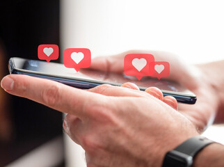 person getting likes on social media, close-up of hands holding smartphone with heart icons...