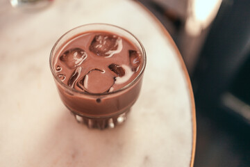 Glass of cold chocolate milk drink on a white marble table.