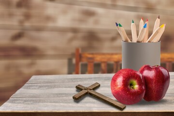 Fresh ripe green apple, Christian cross and jar of pencils on wood school desk