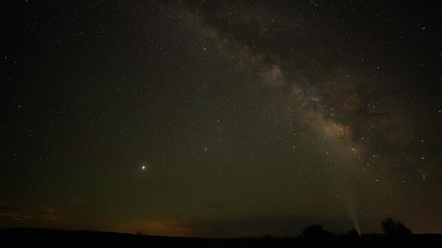 Time lapse shot of Milky Way Galaxy at dark sky with spotlight in background