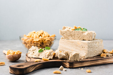 Pieces of sunflower and peanut halva and mint leaves on a cutting board on the table. Caloric oriental dessert