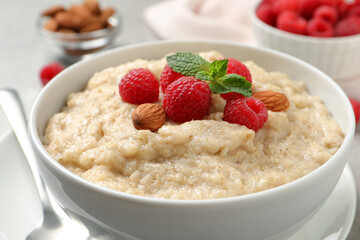 Tasty oatmeal porridge with raspberries and almond nuts in bowl on table, closeup