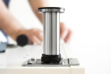 Kitchen installation, worker twists legs for box.Installing the metal cabinet feet. Man's hand repairs furniture in the house