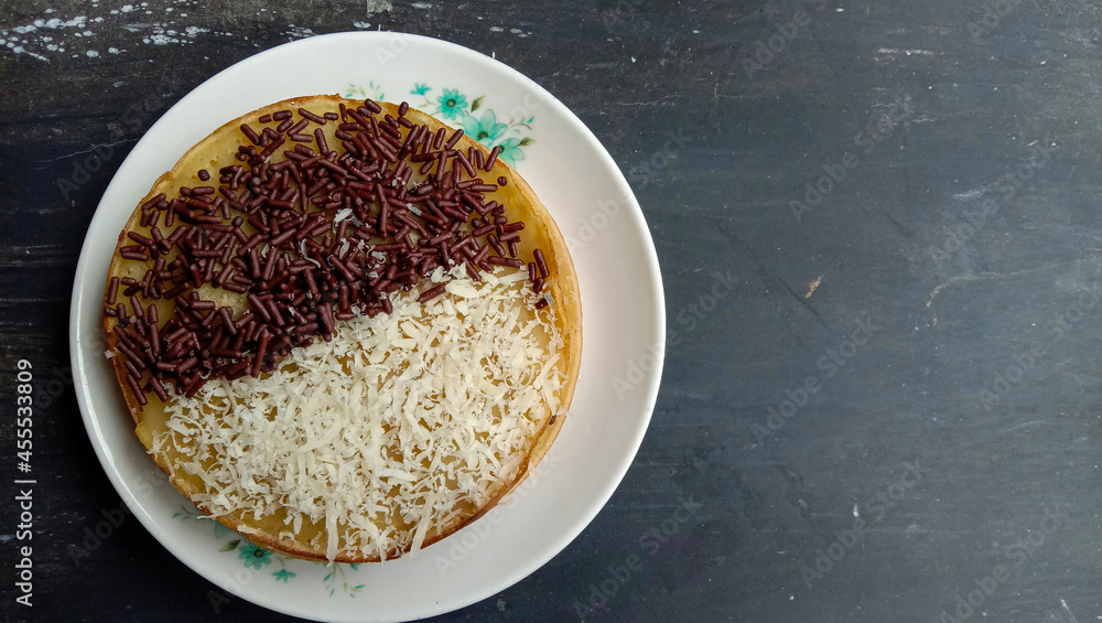 Poster top view of martabak manis on a white plate on a gray wooden background with copy space on the right