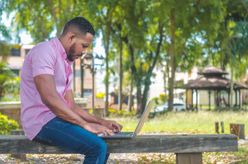 Active dark-haired man of Dominican origin working with a laptop in the park outdoors
