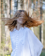 Portrait of a young beautiful blonde girl in a white blouse with strongly developing hair in the park.