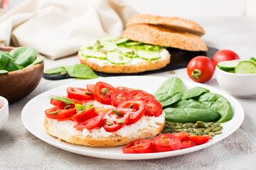 Delicious bagel stuffed with feta, tomatoes and pumpkin seeds and spinach leaves on a plate. Light Healthy Vitamin Snack. Close-up