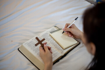 Closeup of bible and woman hand holding a pencil and write something.