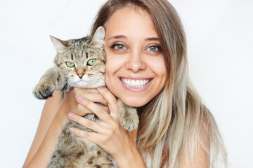 A young charming blonde woman with a beautiful smile and dimples holds a Tabby cat with green eyes isolated on a white background. Good friends. Friendship of a pet and its owner. Close-up