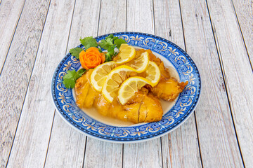 Chinese recipe for breaded and fried chicken fillets, sent chopped on a blue plate with Chinese lemon sauce with carrot flower