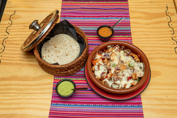 Mexican beef alambre recipe with lots of melted cheese, guacamole and mole sauce, corn tortillas in clay and wicker containers