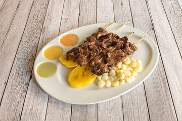 tray of typical plate of Peruvian anticuchos grilled on charcoal grilled skewers with cooked potatoes and corn with sauces