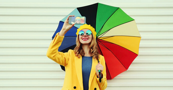 Portrait of happy smiling young woman taking a selfie picture by phone holding colorful umbrella on white background
