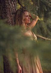 Romantic fairy makeup beautiful emotional blond woman posing in fashion gold color dress near the trunk of tree on summer background outside . Closeup
