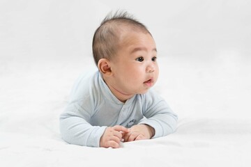 Morning Time.Adorable newborn kid during tummy time smiling happily at home.Portrait of cute smiling happy asian baby boy crawling on bed on the white blanket in bedroom.