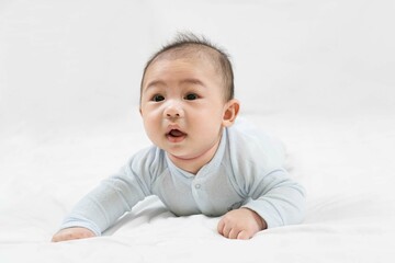 Morning Time.Adorable newborn kid during tummy time smiling happily at home.Portrait of cute smiling happy asian baby boy crawling on bed on the white blanket in bedroom.