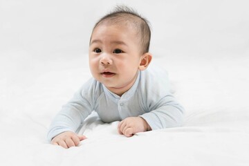 Morning Time.Adorable newborn kid during tummy time smiling happily at home.Portrait of cute smiling happy asian baby boy crawling on bed on the white blanket in bedroom.